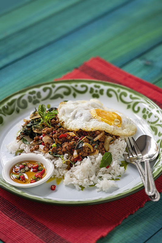 著名的泰国辣菜“Pak Krapao Moo”在英语中是用神圣罗勒炸猪肉，在一个古老的绿松石色风化木桌上用蒸饭和煎蛋和“Pik Nam Bla”(鱼酱辣椒)。